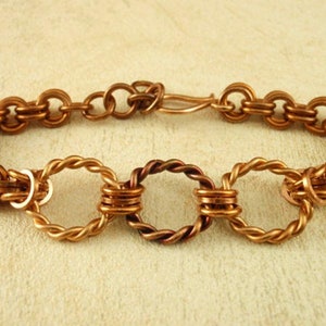 May include: A copper bracelet with a chain link design and three twisted wire rings. The bracelet has a lobster clasp closure.
