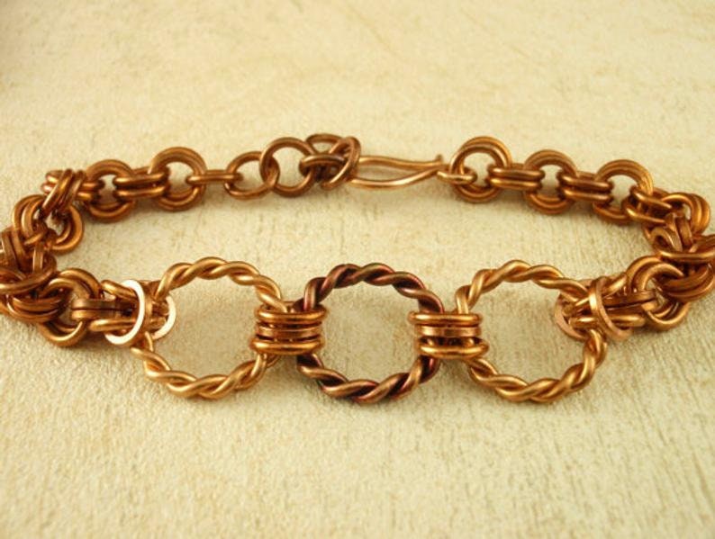 May include: A copper bracelet with a chain link design and three twisted wire rings. The bracelet has a lobster clasp closure.
