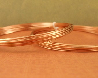 May include: Two circular coils of shiny, metallic copper wire. The wire is thin, smooth, and wound into multiple concentric loops. A small, white plastic zip tie secures the coils together, maintaining their circular shape and structure.