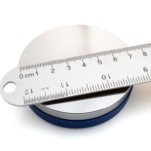 May include: A silver metal disc with a blue base is measured with a ruler. The ruler shows measurements in inches and centimeters. The disc is approximately 4 inches in diameter.
