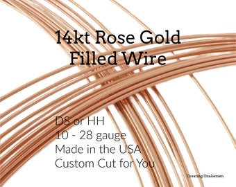 May include: A coil of 14kt rose gold filled wire. The text on the image reads: 14kt Rose Gold Filled Wire, DS or HH, 10 - 28 gauge, Made in the USA, Custom Cut for You, Creating Unakemen. The wire is thin, metallic, and has a copper-toned finish.