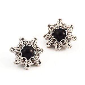 Könnte beinhalten: Ein Paar silberne sternförmige Ohrringe mit schwarzen Edelsteinen in der Mitte.