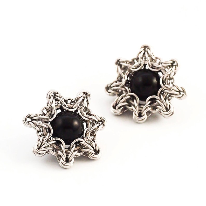 K&ouml;nnte beinhalten: Ein Paar silberne sternf&ouml;rmige Ohrringe mit schwarzen Edelsteinen in der Mitte.