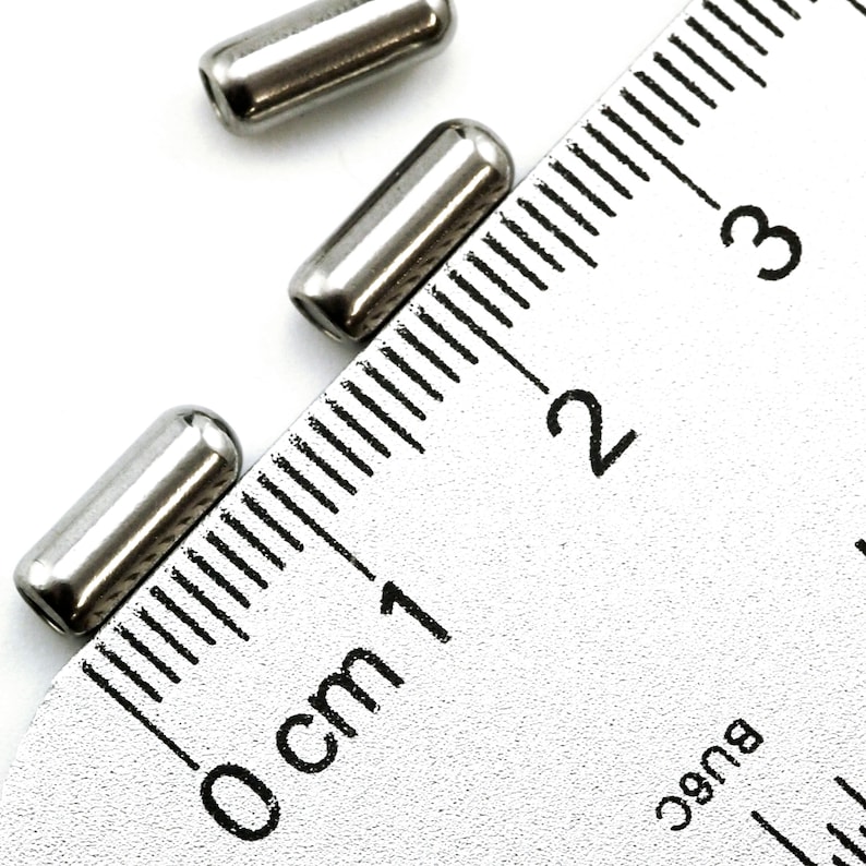 May include: Three silver metal tubes, each measuring approximately 1 cm in length, are placed on a ruler with markings in centimeters. The ruler shows measurements from 0 cm to 3 cm.