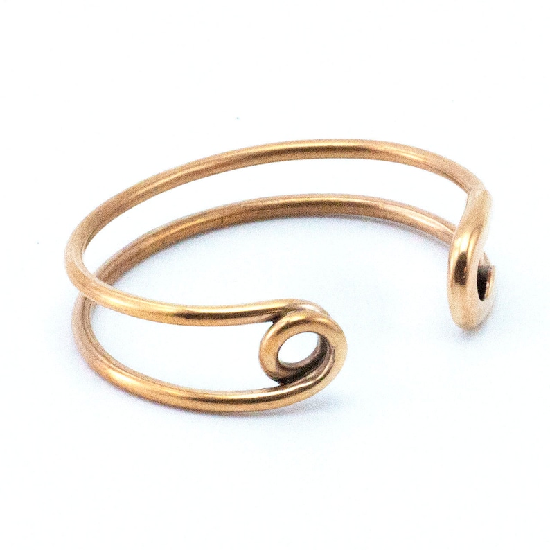 K&ouml;nnte beinhalten: Ein goldfarbenes Metallarmband mit einem Sicherheitsnadelverschluss. Das Armband besteht aus zwei d&uuml;nnen Dr&auml;hten, die miteinander verdreht sind.