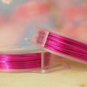 K&ouml;nnte beinhalten: Zwei durchsichtige Kunststoffspulen, die mit leuchtend metallisch pinkfarbenem Basteldraht umwickelt sind. Die Spulen sind leicht versetzt gestapelt und zeigen die reflektierende, glatte Textur des d&uuml;nnen, flexiblen Drahtes, der ordentlich aufgewickelt ist.