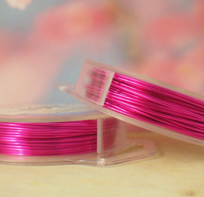 K&ouml;nnte beinhalten: Zwei durchsichtige Kunststoffspulen, die mit leuchtend metallisch pinkfarbenem Basteldraht umwickelt sind. Die Spulen sind leicht versetzt gestapelt und zeigen die reflektierende, glatte Textur des d&uuml;nnen, flexiblen Drahtes, der ordentlich aufgewickelt ist.