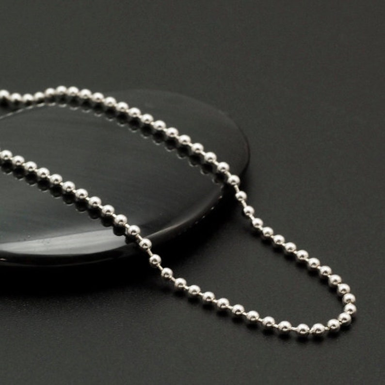 May include: A silver ball chain necklace with a smooth, polished finish. The chain is made of small, round beads that are evenly spaced.