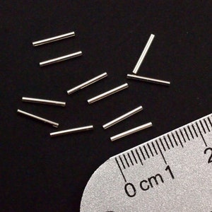Pu&ograve; includere: Primo piano di un gruppo di anelli di salto in metallo argentato, sparsi su una superficie nera. Un righello &egrave; parzialmente visibile nell'angolo in basso a destra dell'immagine, con la misura 0 cm segnata su di esso.