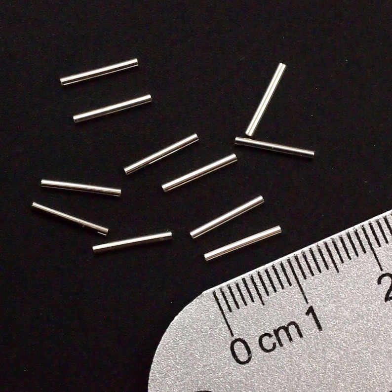 Pu&ograve; includere: Primo piano di un gruppo di anelli di salto in metallo argentato, sparsi su una superficie nera. Un righello &egrave; parzialmente visibile nell'angolo in basso a destra dell'immagine, con la misura 0 cm segnata su di esso.