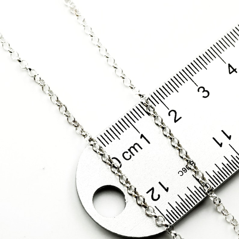 Puede incluir: Una delicada cadena de plata con peque&ntilde;os eslabones circulares se muestra junto a una regla met&aacute;lica. La regla est&aacute; marcada en cent&iacute;metros, con la cadena extendi&eacute;ndose hasta la marca de 4 cm. El fondo es blanco.