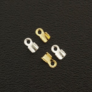 May include: Four metal clasps for jewelry making, two gold and two silver. The clasps have a small loop at the top and a flat, slightly curved bottom.