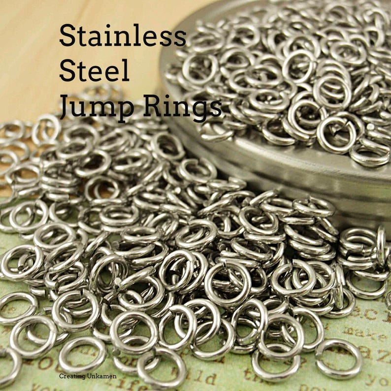 Puede incluir: Una gran colecci&oacute;n de peque&ntilde;as anillas de salto de acero inoxidable de color plateado. Los anillos met&aacute;licos son circulares con una abertura visible en cada pieza. El texto "Stainless Steel Jump Rings" aparece impreso en negro.