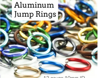Puede incluir: Una colección de anillas de salto de aluminio multicolor en varios tonos, incluyendo rojo, azul, verde, dorado y plateado. El texto Aluminum Jump Rings y 12 gauge 10mm ID es visible. Estos conectores metálicos circulares tienen una abertura.