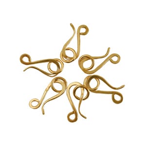 May include: Six gold-colored metal S-hook clasps arranged in a circular pattern. Each clasp features a smooth, curved wire design with a circular loop at one end and a hook at the other, creating a functional fastener for jewelry or craft projects.
