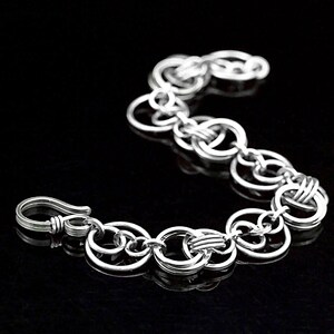 May include: A silver bracelet composed of linked circular elements. The bracelet has a hook clasp. The design is simple and elegant, suitable for everyday wear. The bracelet is displayed against a black background. The bracelet's length is approximately 18 cm.