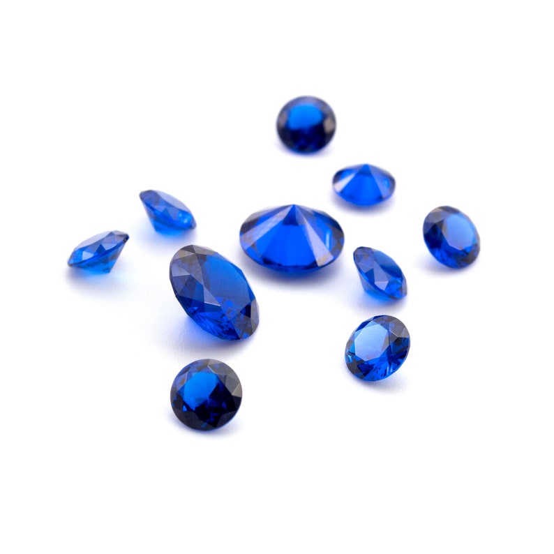 May include: A collection of ten blue gemstones, some round and some faceted, scattered on a white background.
