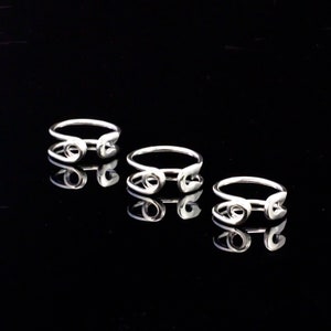 K&ouml;nnte beinhalten: Drei silberne Ringe mit einem Sicherheitsnadel-Design. Die Ringe sind auf einer schwarzen Oberfl&auml;che gestapelt.