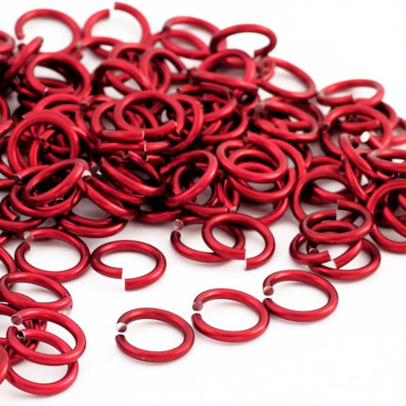 May include: A large pile of red metal jump rings. The rings are small and round, and they are all the same size.