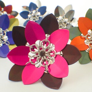 May include: A close-up of a multi-colored flower-shaped metal object. The flower has eight petals, with alternating colors of pink and brown. The center of the flower is made of silver chainmail.
