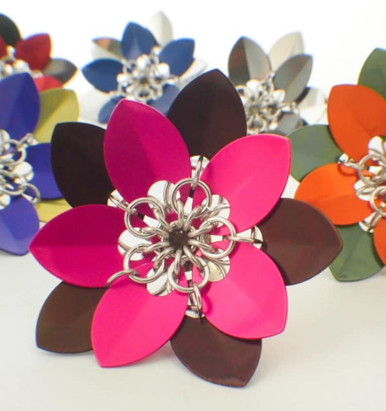 May include: A close-up of a multi-colored flower-shaped metal object. The flower has eight petals, with alternating colors of pink and brown. The center of the flower is made of silver chainmail.