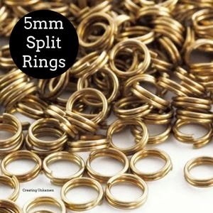 May include: A close-up of a pile of 5mm gold split rings. The rings are made of metal and are used for jewelry making.