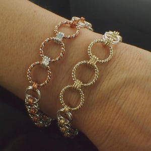 May include: Two chainmaille bracelets featuring interlocking circular links. One bracelet combines copper and silver-toned twisted wire rings, while the other bracelet features gold-toned and silver-toned twisted wire rings in a repeating pattern.