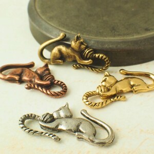 Puede incluir: Cuatro abalorios de gato de metal con un dise&ntilde;o de cuerda. Los gatos son de diferentes colores: oro, cobre, plata y lat&oacute;n.
