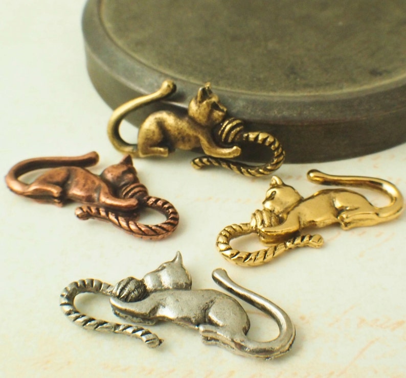 Puede incluir: Cuatro abalorios de gato de metal con un dise&ntilde;o de cuerda. Los gatos son de diferentes colores: oro, cobre, plata y lat&oacute;n.