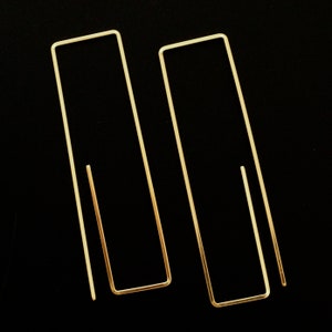 May include: Two gold-toned metal earrings, each shaped like a rectangle with a slightly rounded corner. The earrings are simple and minimalist in design.