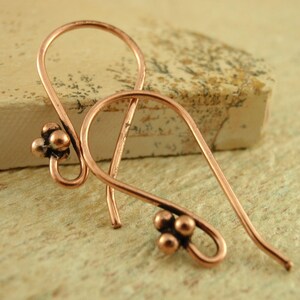 May include: A pair of copper earrings with a teardrop shape and three small beads at the bottom of each earring.