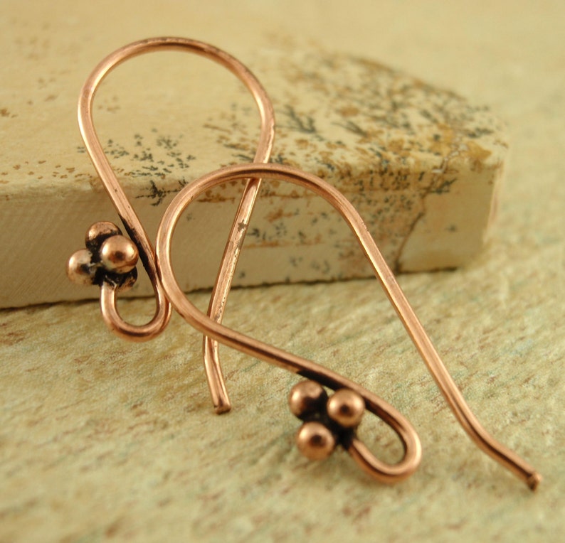 May include: A pair of copper earrings with a teardrop shape and three small beads at the bottom of each earring.