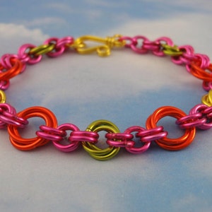 K&ouml;nnte beinhalten: Ein Kettenarmband aus ineinandergreifenden Metallringen in leuchtenden Farben wie Pink, leuchtendem Orange und Limettengr&uuml;n. Das Armband verf&uuml;gt &uuml;ber einen goldfarbenen S-Haken-Verschluss, der die kreisf&ouml;rmigen Glieder zu einer Schlaufe verbindet.