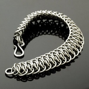 May include: A silver chain bracelet with a woven design. The bracelet is made of small, interlocking metal rings.