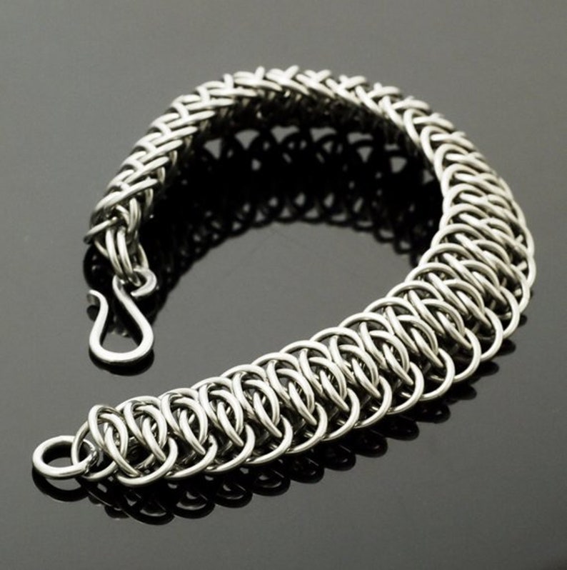 May include: A silver chain bracelet with a woven design. The bracelet is made of small, interlocking metal rings.