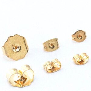 May include: Five gold-colored earring backs. The backs are made of metal and have different shapes and sizes.