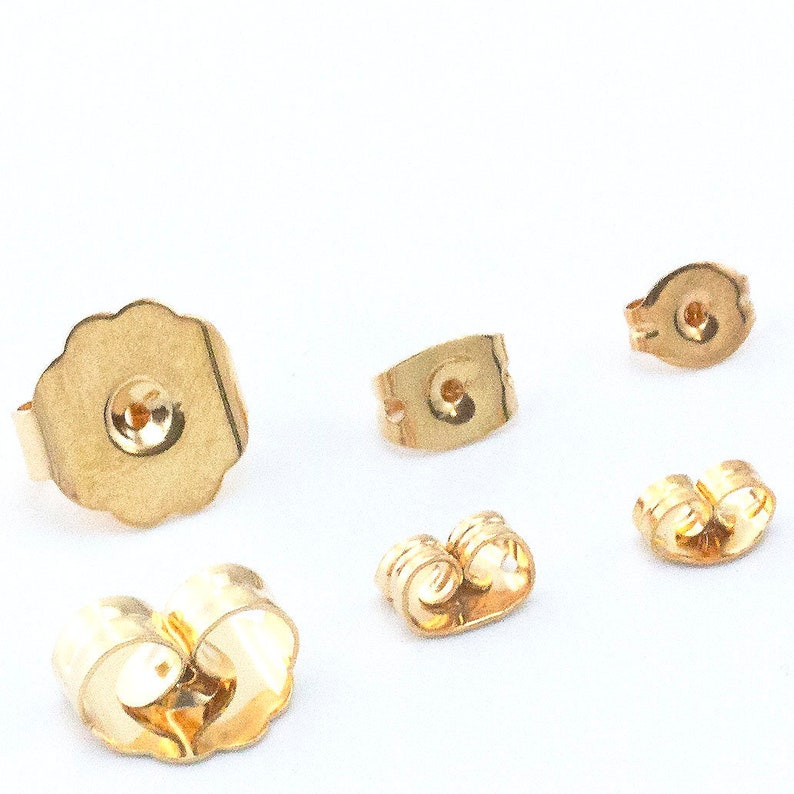 May include: Five gold-colored earring backs. The backs are made of metal and have different shapes and sizes.