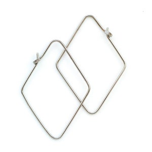 May include: A pair of silver square hoop earrings. The earrings are made of thin metal and have a simple, modern design.