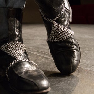 Pode incluir: Botas de couro preto com detalhes de corrente prateada em torno dos tornozelos.