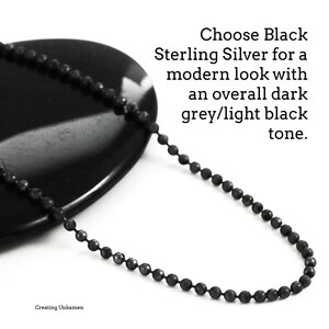 May include: A black sterling silver chain necklace with a ball chain design. The chain is on a black stone surface. Choose Black Sterling Silver for a modern look with an overall dark grey/light black tone.