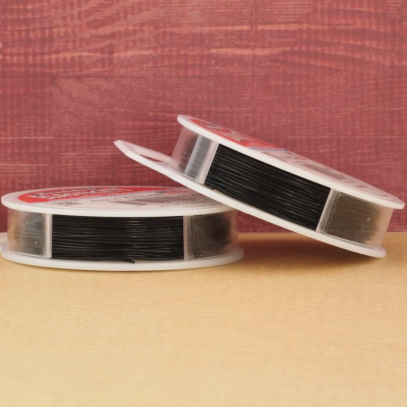May include: Two spools of black elastic cord, each in a clear plastic container with a white label. The spools are stacked on top of each other.