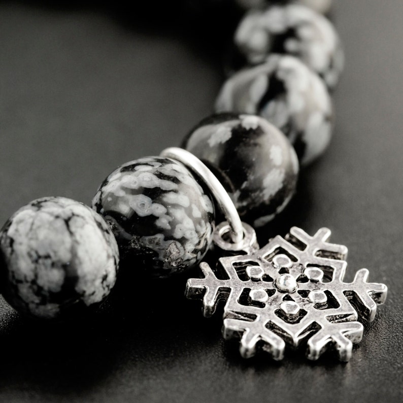 May include: A black and white snowflake charm bracelet with a silver snowflake pendant. The bracelet is made of round, black and white speckled beads.