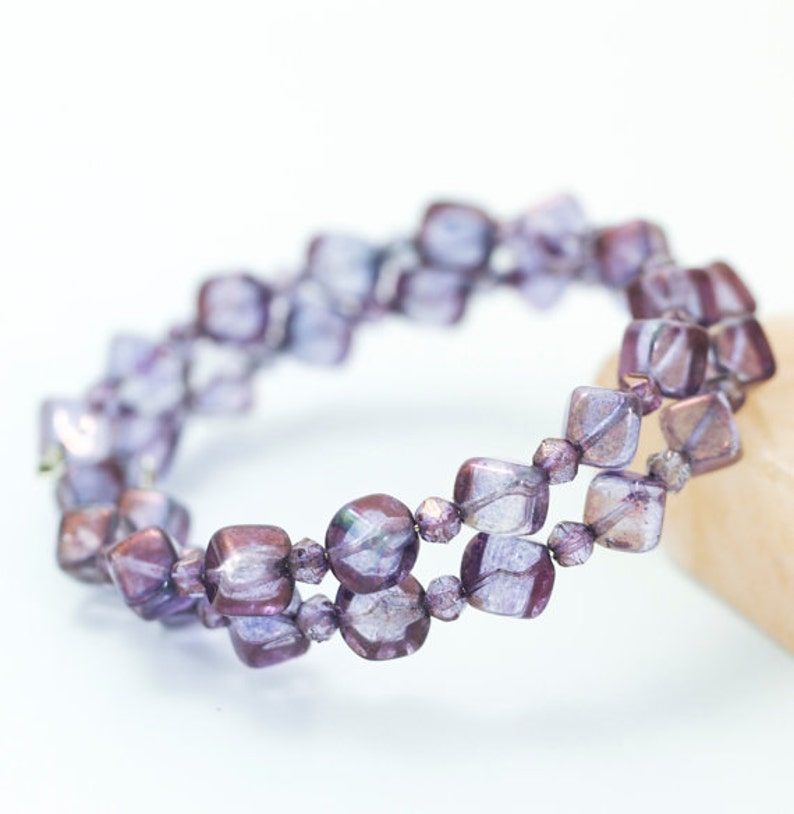 May include: A double-strand bracelet made of iridescent purple glass beads. The beads are square-shaped and have a slightly textured surface.