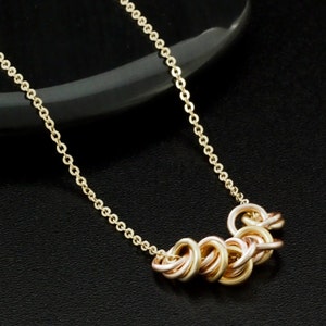 May include: A gold chain necklace with a cluster of interlocked rings in a rose gold finish.