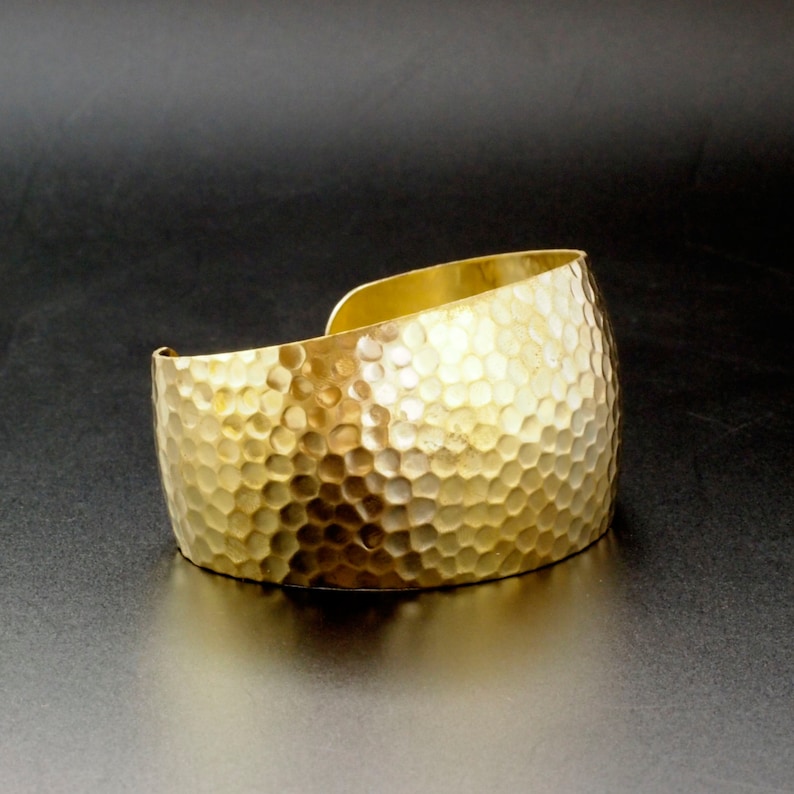 以下が含まれることがあります： 金色のハンマーで叩かれた金属製のバングル。バングルは厚い金属でできており、ハンマーで叩かれた質感があります。