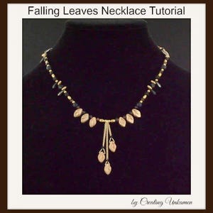 Könnte beinhalten: Eine goldene Halskette mit schwarzen Perlen und goldenen Blatt-Anhängern. Die Halskette hat einen Anhänger mit einer Gruppe von goldenen Blatt-Anhängern, die daran hängen. Die Halskette befindet sich auf einem schwarzen Hintergrund.  Falling Leaves Necklace Tutorial by Creating Ukamen