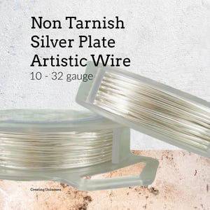 Peut inclure: Deux bobines en plastique transparent contenant du fil artistique argenté non ternissable. Le texte sur l'image indique : Non Tarnish Silver Plate Artistic Wire 10 - 32 gauge. Le fil est de couleur argent métallique et enroulé sur les bobines.