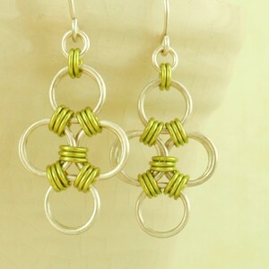May include: Silver earrings with a green chainmail design. The earrings are made of multiple interlocking rings.