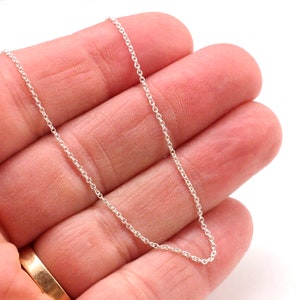 May include: A silver chain necklace with a delicate, thin design. The chain is shown lying on a hand, with the ends of the chain visible.