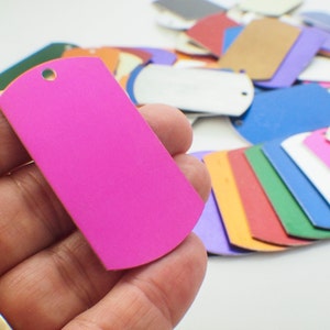 May include: A bright pink metal dog tag with a rounded edge and a small hole at the top. The tag is being held in a hand.